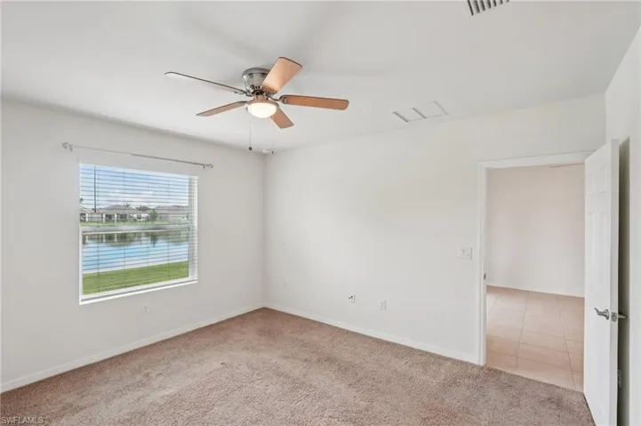 Unfurnished room with light carpet, a water view, ceiling fan, and light tile patterned floors