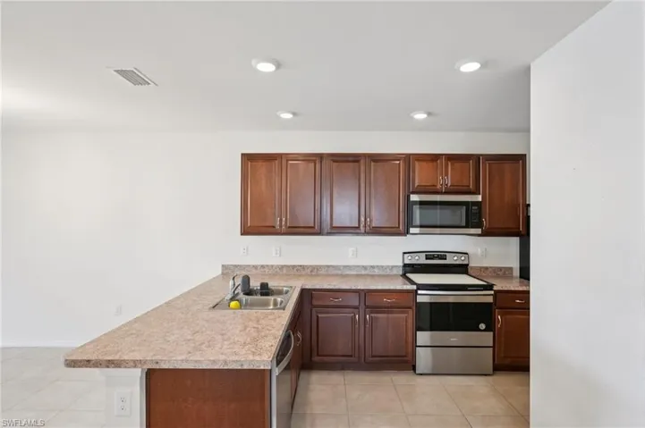 Kitchen with stainless steel appliances, light countertops, a peninsula, light tile patterned floors, and recessed lighting