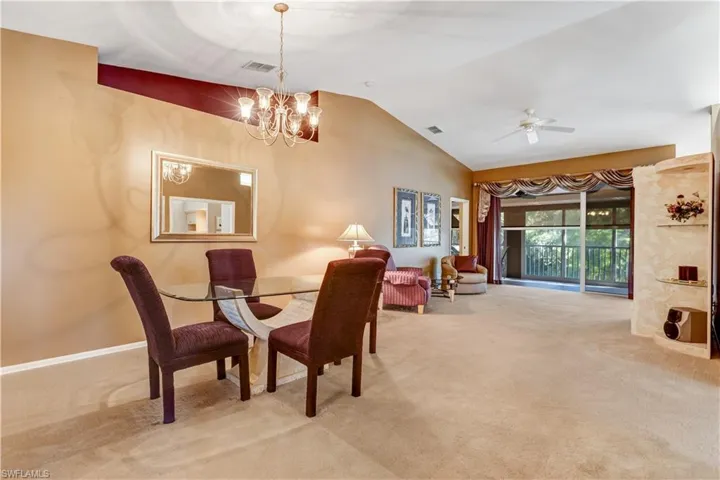 Dining space featuring light colored carpet, lofted ceiling, a chandelier, and ceiling fan