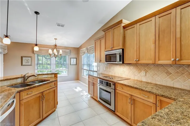 Kitchen with light stone counters, lofted ceiling, appliances with stainless steel finishes, a chandelier, and decorative light fixtures