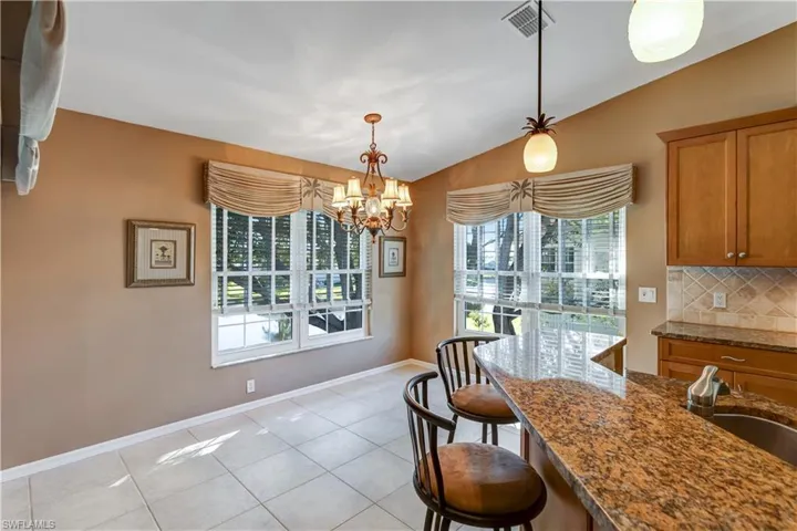 Kitchen featuring lofted ceiling, dark stone counters, brown cabinetry, light tile patterned flooring, and a kitchen bar