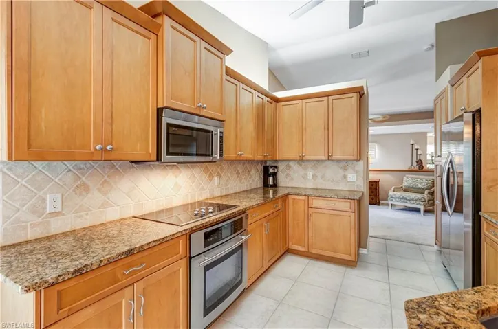 Kitchen with appliances with stainless steel finishes, light stone counters, tasteful backsplash, light tile patterned floors, and a ceiling fan