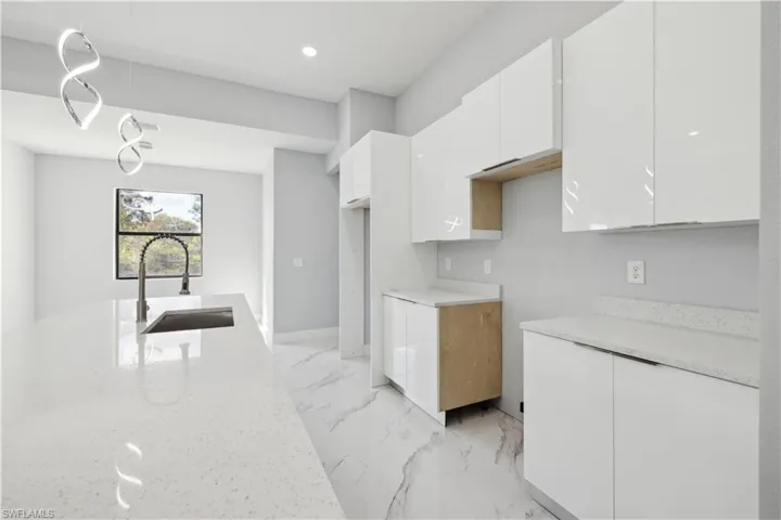 Kitchen featuring white cabinets, light stone counters, and sink