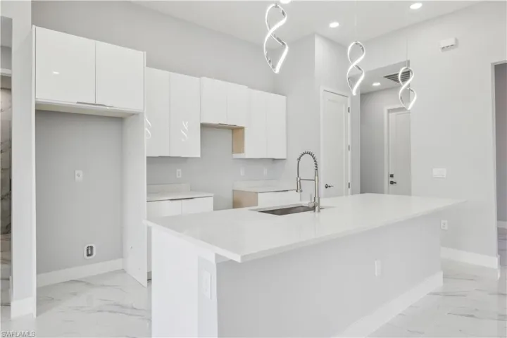 Kitchen with white cabinetry, a center island with sink, and sink