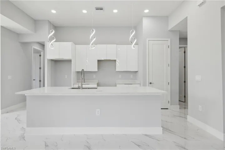 Kitchen with sink, decorative light fixtures, white cabinetry, and an island with sink