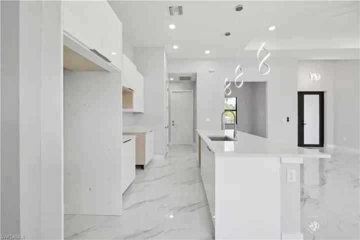 Kitchen with sink, white cabinetry, hanging light fixtures, and an island with sink