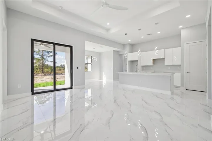 Unfurnished living room with a tray ceiling, ceiling fan, and sink