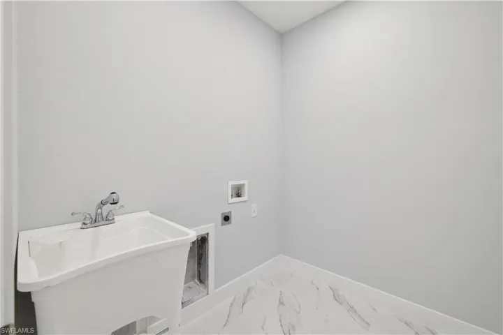 Clothes washing area featuring hookup for an electric dryer, washer hookup, and sink