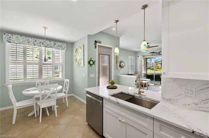 Kitchen featuring stainless steel dishwasher, a peninsula, light stone countertops, white cabinetry, and backsplash