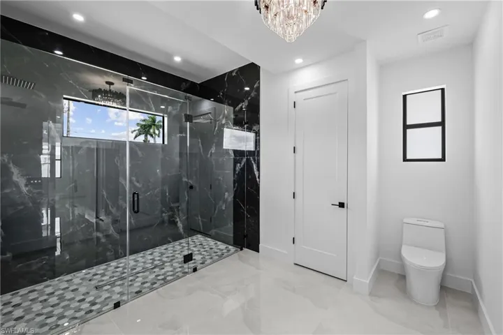 Bathroom with a shower with shower door, toilet, and a notable chandelier