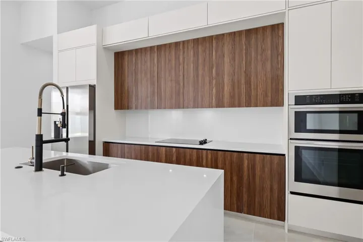 Kitchen featuring black electric stovetop, light tile patterned floors, sink, double oven, and white cabinets