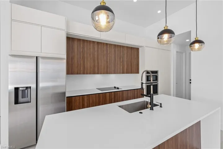 Kitchen with stainless steel refrigerator with ice dispenser, hanging light fixtures, sink, white cabinetry, and black electric cooktop