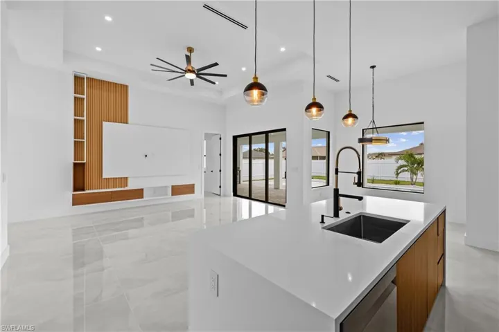 Kitchen featuring dishwasher, decorative light fixtures, sink, ceiling fan, and a center island with sink