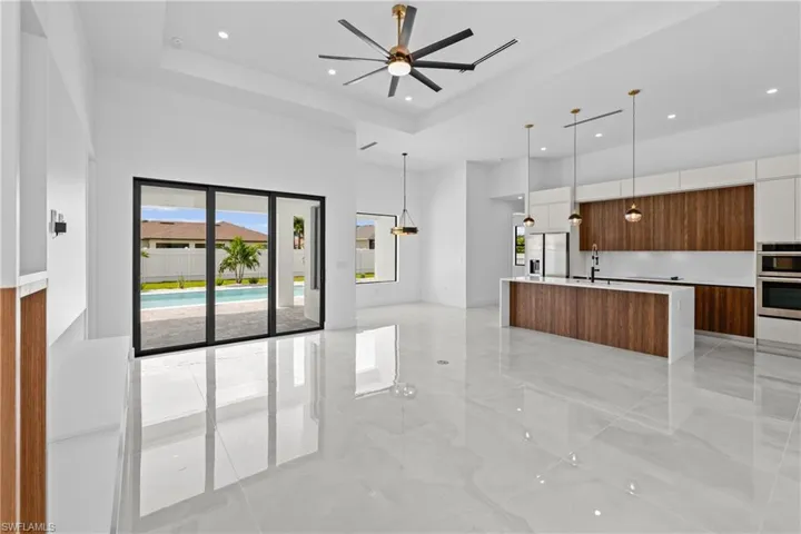 Kitchen featuring a kitchen island with sink, sink, ceiling fan, hanging light fixtures, and white cabinets