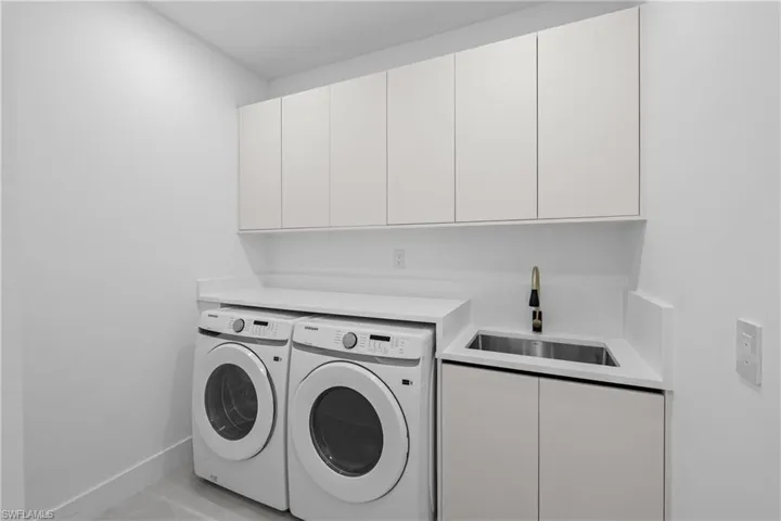 Washroom with cabinets, washing machine and clothes dryer, and sink