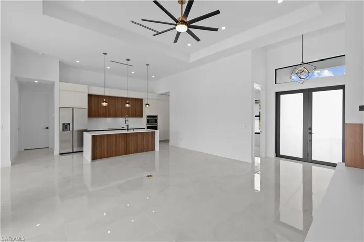 Kitchen with decorative light fixtures, appliances with stainless steel finishes, white cabinetry, an island with sink, and ceiling fan