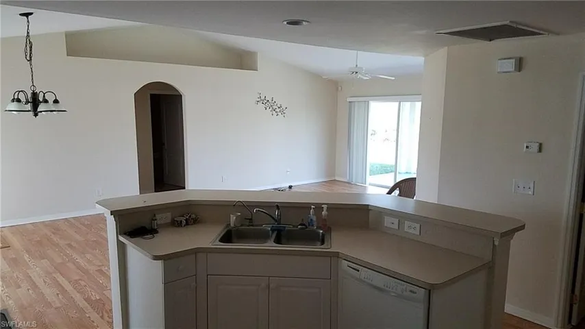 Kitchen island with a dual-basin sink, vaulted ceilings, wood-finish flooring, recessed architectural detailing, and an arched doorway