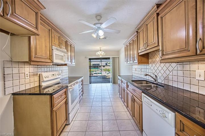 Galley Kitchen with raised wood panel cabinetry, tile backsplash, eat in dining area and pocket slider to the pool.