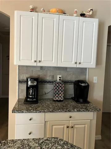 Kitchen featuring decorative backsplash, white cabinetry, dark wood-type flooring, and dark stone counters