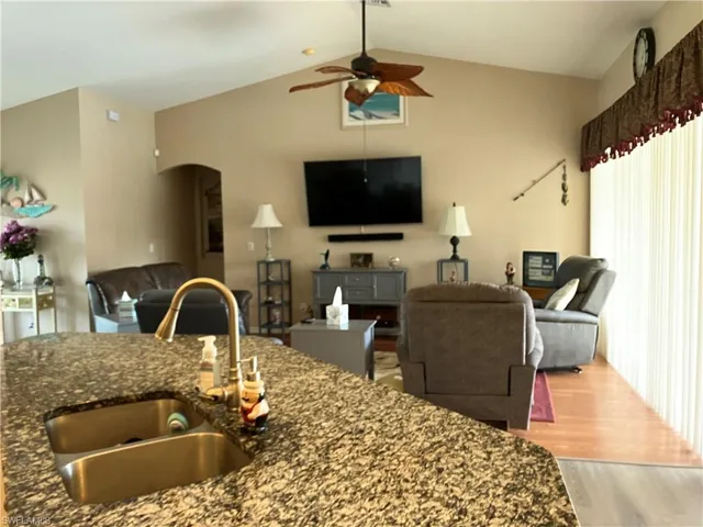 Kitchen with lofted ceiling, ceiling fan, light wood-type flooring, dark stone countertops, and sink