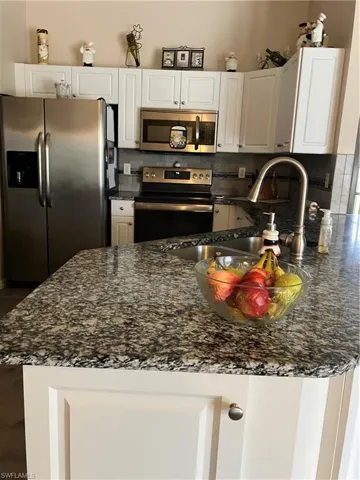 Kitchen featuring appliances with stainless steel finishes, white cabinets, and dark stone countertops