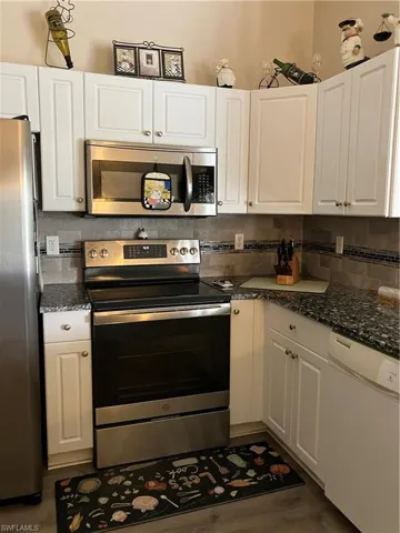 Kitchen with hardwood / wood-style flooring, stainless steel appliances, tasteful backsplash, and white cabinets