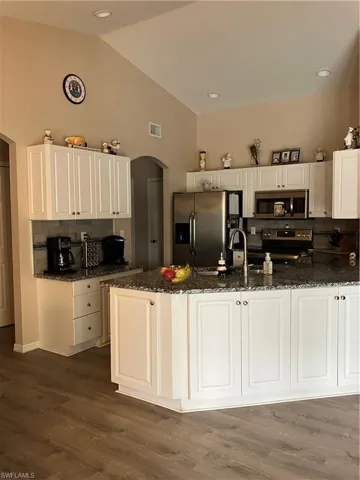 Kitchen with white range, decorative backsplash, dark hardwood / wood-style floors, dark stone counters, and stainless steel refrigerator