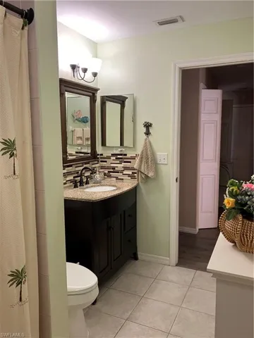 Bathroom featuring toilet, a shower with curtain, vanity, decorative backsplash, and tile patterned flooring