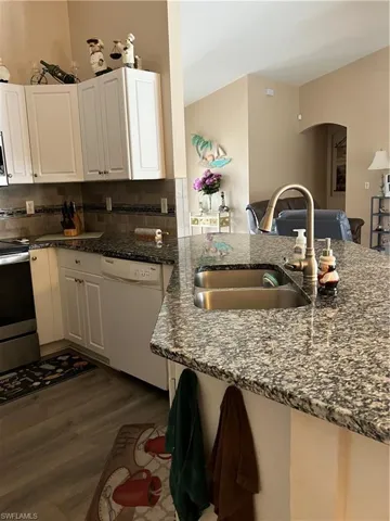 Kitchen featuring sink, dishwasher, white cabinetry, and dark wood-type flooring