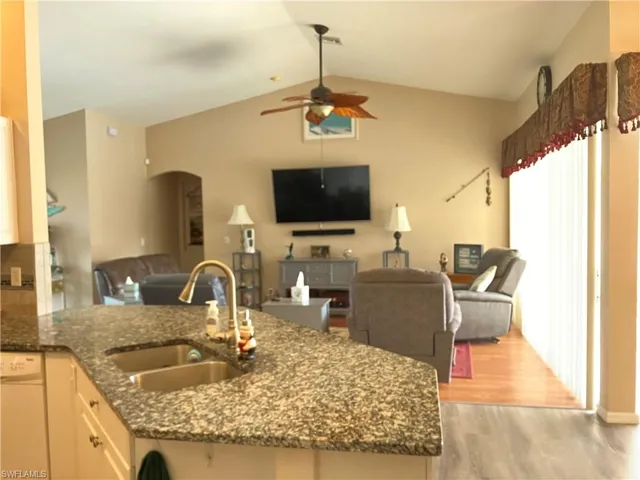 Kitchen featuring sink, white dishwasher, vaulted ceiling, dark stone counters, and light hardwood / wood-style flooring