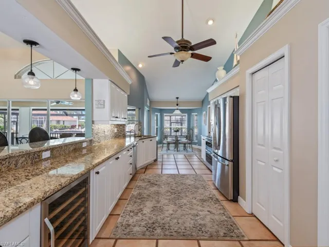 Kitchen featuring decorative light fixtures, white cabinets, beverage cooler, appliances with stainless steel finishes, and light stone counters