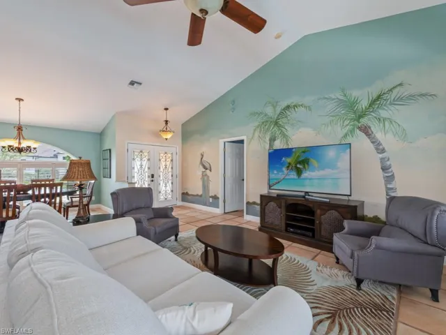 Living area with french doors, light tile patterned floors, ceiling fan, high vaulted ceiling, and a chandelier