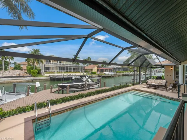Swimming pool with boat lift, a boat dock, a water view, a sunroom, and a patio