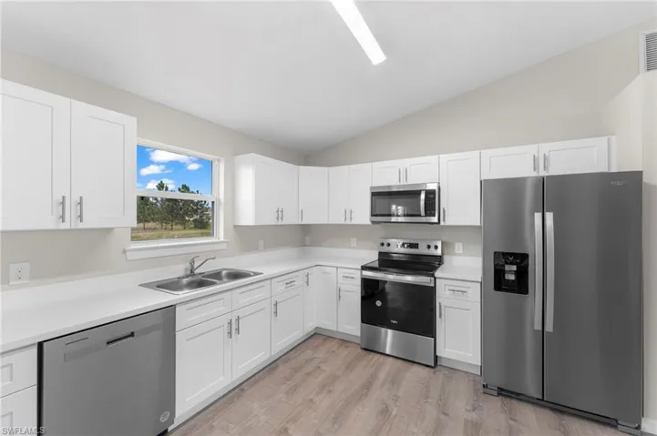 Kitchen featuring appliances with stainless steel finishes, vaulted ceiling, white cabinetry, and sink