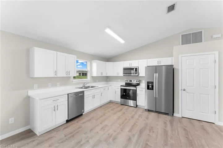 Kitchen with stainless steel appliances, vaulted ceiling, sink, light hardwood / wood-style floors, and white cabinetry