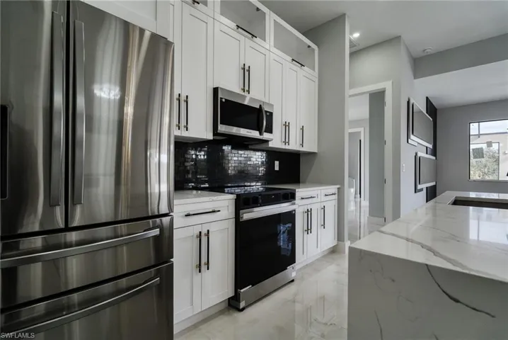 Kitchen featuring appliances with stainless steel finishes, light stone countertops, and white cabinetry