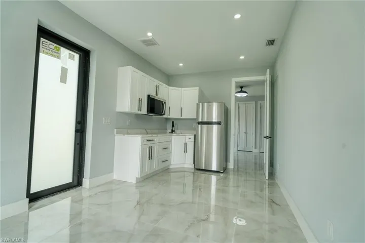 Kitchen featuring white cabinets, appliances with stainless steel finishes, light marble finish flooring, recessed lighting, and light stone counters