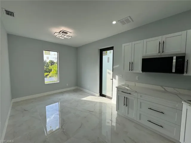 Kitchen featuring light stone countertops, white cabinets, stainless steel microwave, light marble finish floors, and recessed lighting