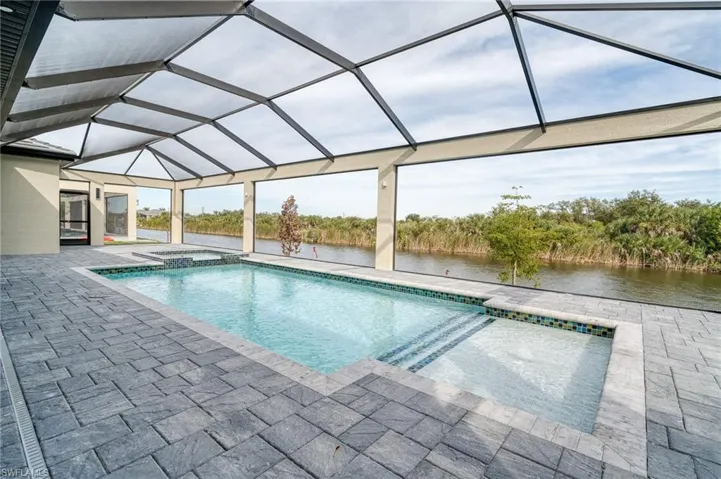 View of pool featuring a lanai, a sunroom, a pool with connected hot tub, a water view, and a patio