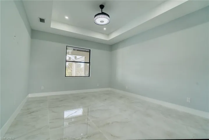 Spare room featuring light marble finish flooring, a tray ceiling, and recessed lighting