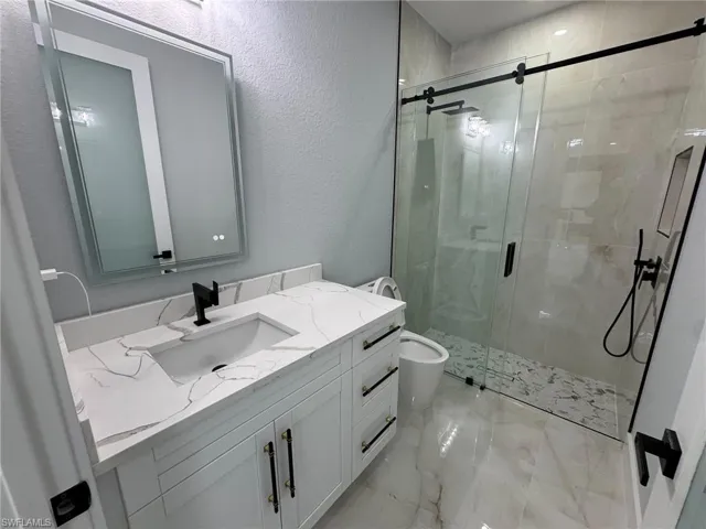 Bathroom featuring vanity, a textured wall, a shower stall, and light marble finish floors