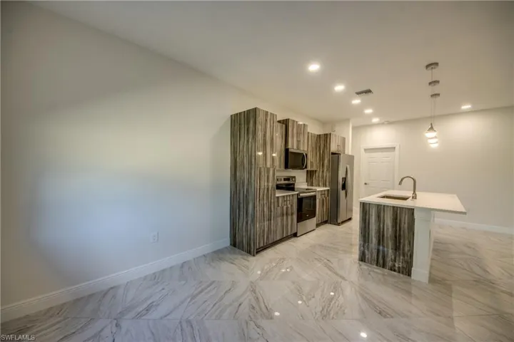 Kitchen featuring modern cabinets, stainless steel appliances, hanging light fixtures, a kitchen island with sink, and light stone countertops