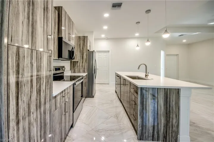 Kitchen featuring modern cabinets, stainless steel appliances, a center island with sink, pendant lighting, and light stone countertops