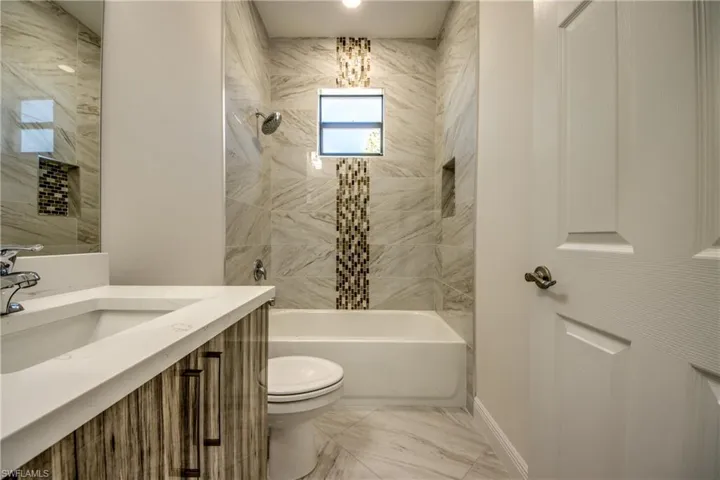 Bathroom featuring bathtub / shower combination, vanity, and light marble finish flooring
