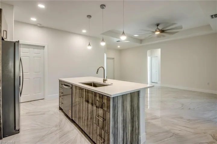 Kitchen featuring stainless steel appliances, hanging light fixtures, open floor plan, an island with sink, and a ceiling fan