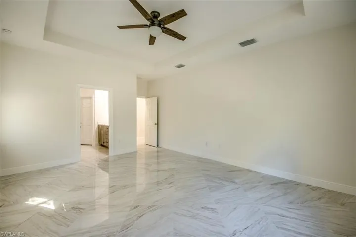 Spare room with a tray ceiling, light marble finish flooring, and a ceiling fan