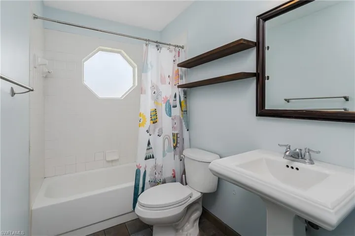 Bathroom featuring a pedestal sink, framed mirror, and wood-finish shelving