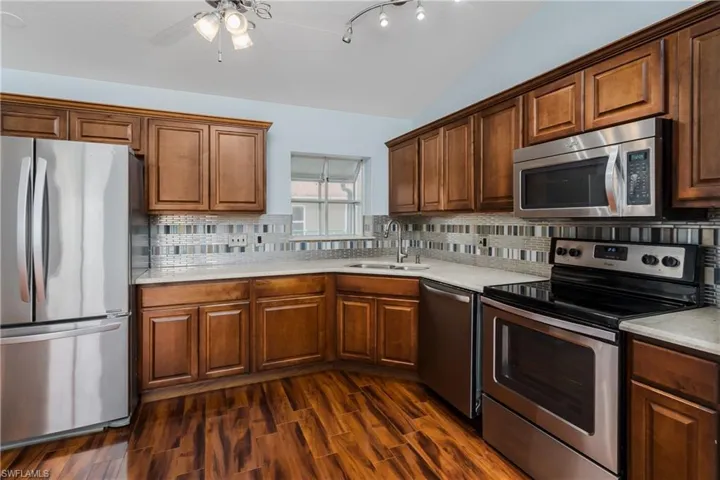 Kitchen featuring stainless steel appliances, wood-finish flooring, wood cabinetry, light-toned countertops, and a tiled backsplash