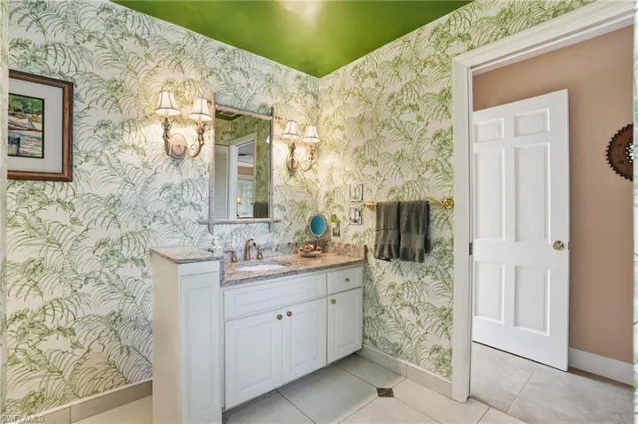 Bathroom with wallpapered walls, light tile patterned flooring, and vanity