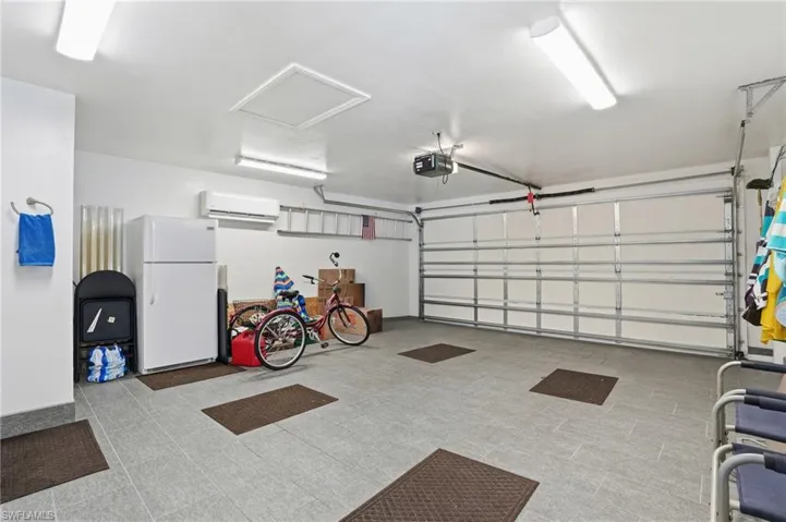 Garage with freestanding refrigerator, an AC wall unit, and a garage door opener